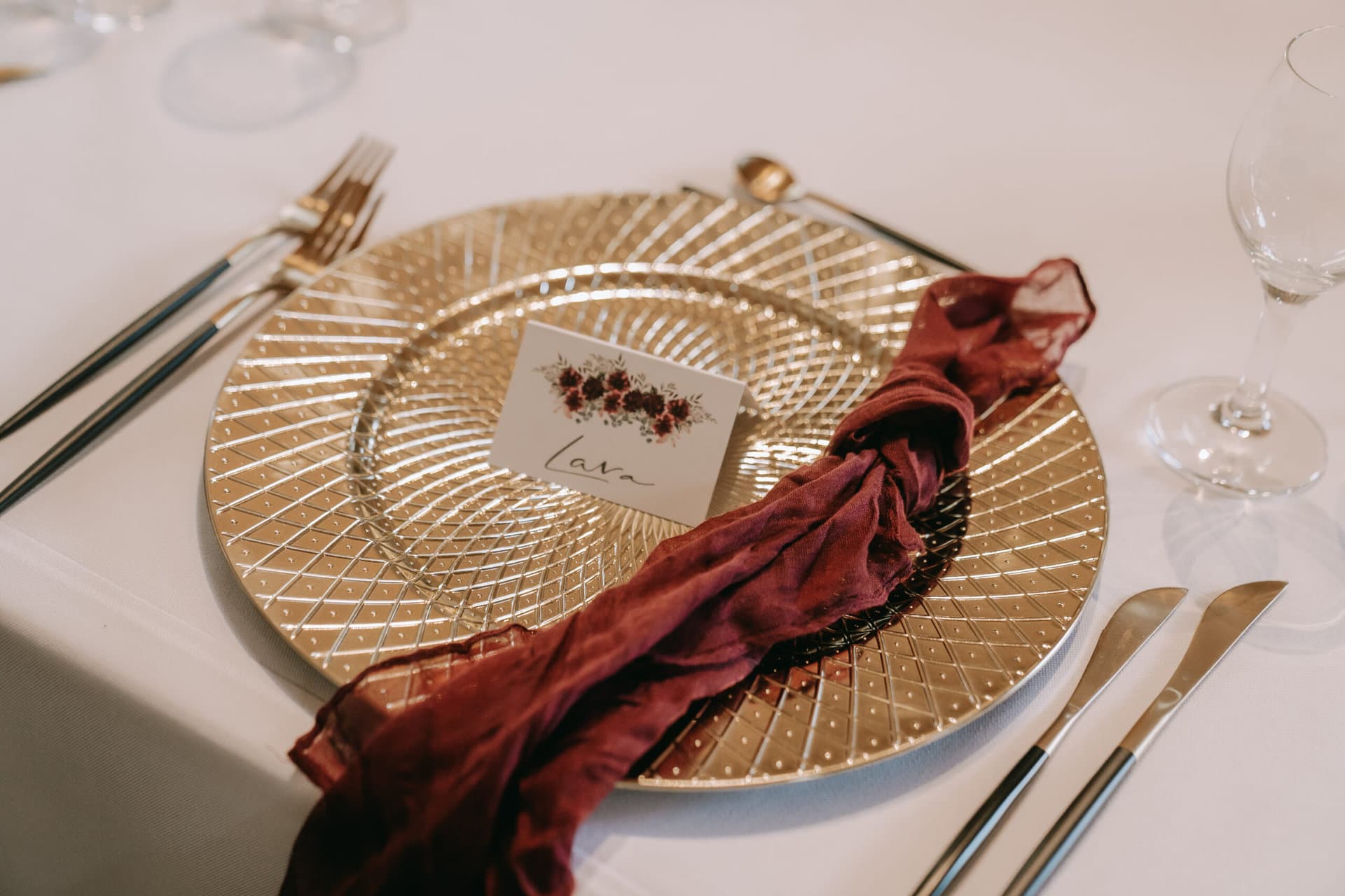 Elegantes Tischgedeck mit einem goldenen Platzteller, Besteck, Weingläsern und einer Tischkarte mit der Aufschrift „Love“.