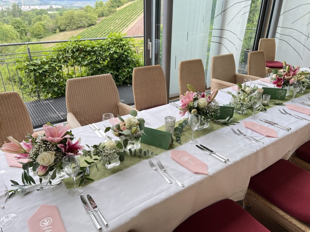 Eleganter Esstisch für eine Hochzeit, dekoriert mit rosa und weißen Blumen, grünen Servietten und mit Blick auf eine üppige Landschaft.